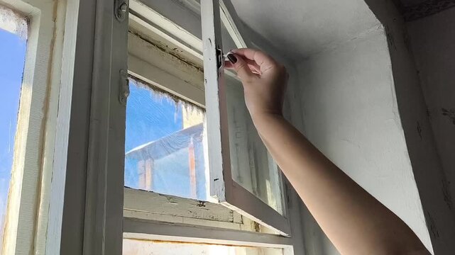 A woman's hand opens the window of an old wooden window. Ventilation of the apartment.