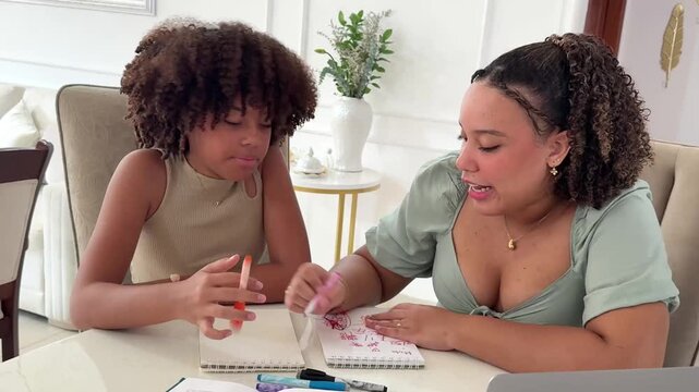An older sister passes on her knowledge while teaching her younger sister to draw in a notebook at home.