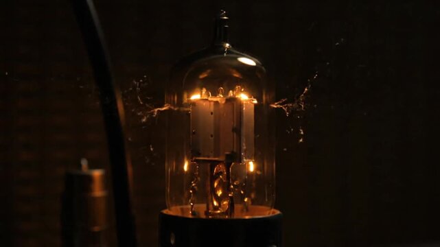 Close-up of a vintage vacuum tube glowing with warm light in a dark setting, showcasing old technology.