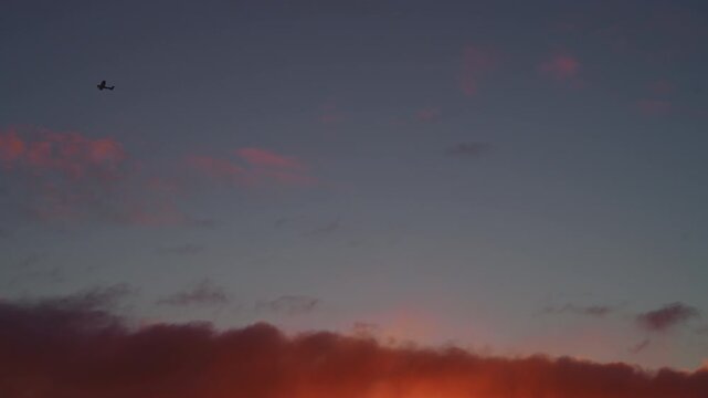 Airplane flying high in the blue sky at sunrise with orange and pink clouds, 4K.