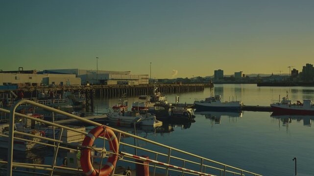 REYKJAVIK, ICELAND - FEBRUARY 8 2026: Industrial harbor ramp with orange lifebuoy and city skyline at golden sunrise, 4K.