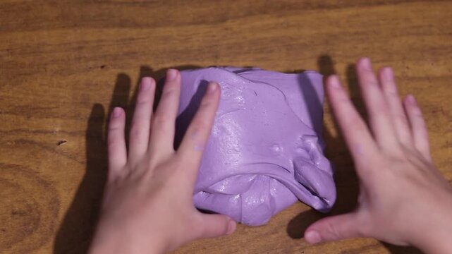 Young hands joyfully stretch and squish vibrant purple slime, providing a satisfying sensory and tactile experience.