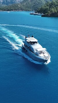 Luxury motor yacht cruising through clear blue waters near a forested coastline