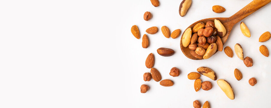 Various nuts: almonds, hazelnuts and brazil nuts in wooden spoon on white background top view. Healthy, delicious food, a source of plant-based protein