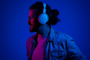 Profile portrait of bearded smiling man in headphones, glasses, blue shirt with neon lights listening to music © Nenad