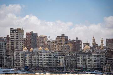Obraz premium Fishing boats moored in the bay in front of high rise buildings along the coast in Alexandria, Egypt