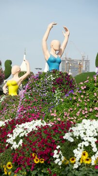 A beautiful spinning statue of a female dancer wearing a large, colorful skirt made entirely of blooming flowers. Creative floral landscaping and topiary art in a public garden