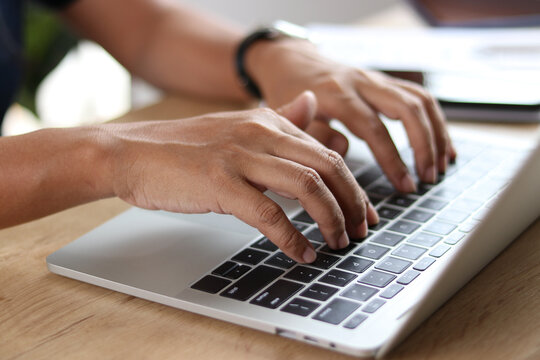 Close-up of professional hands typing on laptop keyboard at wooden desk. Business work, data entry, productivity, remote work, technology, office workspace, and modern working concept.