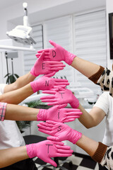 Dental team wearing pink gloves forming the word DENTIST as a symbol of profession and teamwork in clinic.