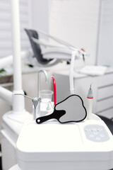Dental unit with mirror and instruments in foreground inside bright modern dental treatment room.