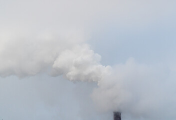 Obraz premium Smoking chimney releasing smoke against a winter sky. Smoke from factory pipe of heat station in the city in winter time. Air pollution. Nuclear power plant cooling. CO2, greenhouse gases emissions. 