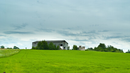 green field and old hay storage building against the background of gray-blue sky