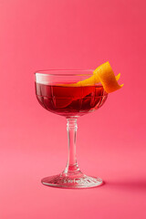 Elegant Red Cocktail with Orange Twist in Coupe Glass on Pink Background