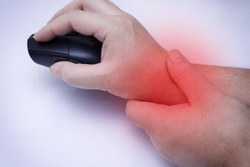 A close-up shot of a person using their other hand to massage a painful wrist while holding a black computer mouse, isolated on a white background and red spot on his wrist
