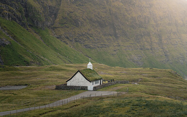 Obraz premium View of traditional nordic church with grass roof in Saksun, Faroe Islands with mountains in background