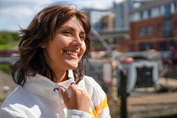 Woman smiles at the docks while wearing a jacket in the daytime sun