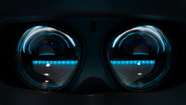 Close-up view of virtual reality headset lenses glowing in dark environment. Futuristic immersive technology concept without people.