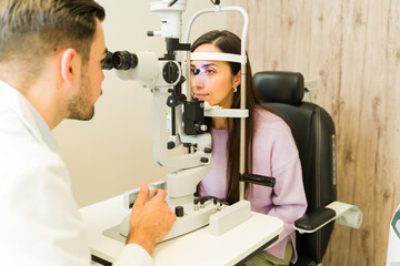 Professional ophthalmologist performing an eye exam on a female patient using a slit lamp for vision and health care