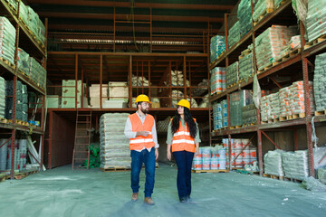 Two construction workers, a man and a woman, wearing hard hats and safety vests, walking and...