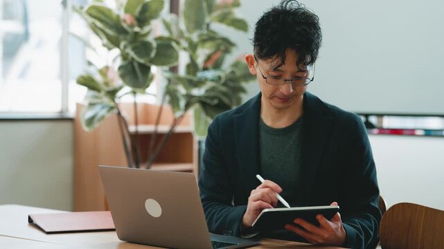 ノートパソコンとタブレットを使って作業する日本人ビジネスマンのオフィスシーン, Japanese businessman working with a laptop and tablet in the office