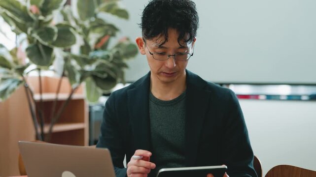 ノートパソコンとタブレットを使って作業する日本人ビジネスマンのオフィスシーン, Japanese businessman working with a laptop and tablet in the office