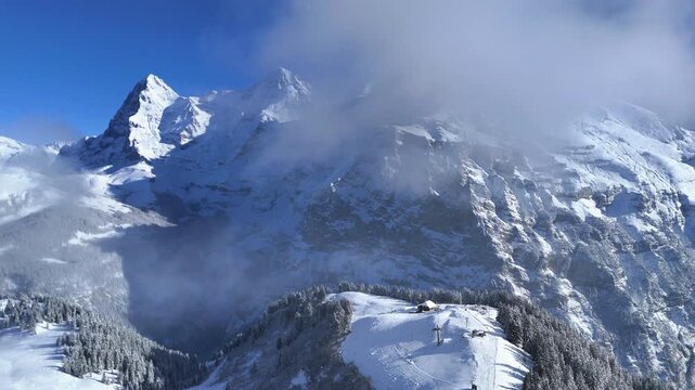Drone video of M&auml;nnlichen in winter, featuring snow-covered ski slopes, alpine terrain, and scenic mountain views in Switzerland.