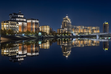 Fototapeta premium Modern buildings, the embankment and the bridge are reflected in the water of the Ishim (Esil) river in Astana, the capital of Kazakhstan