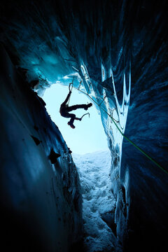 Man climbing frozen ice cave in winter mountains