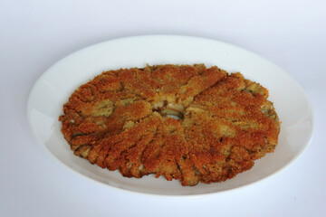 Fried breaded parasol mushroom cap on a white plate showing textured gills on the underside