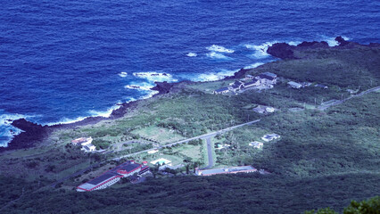 八丈富士の山頂付近から見下ろした青い海と溶岩石の海岸線が続く八丈島の風景