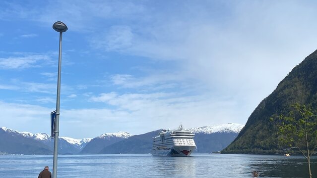 Kreuzfahrtschiff von AIDA Cruises im Hafen von Vik in Norwegen, umgeben von Fjordlandschaft und Bergen. Dokumentarische Reiseszene mit Marke, Wasser und Natur.