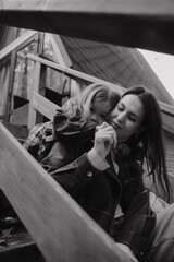 Mother and daughter hugging on the steps of a wooden staircase. A little girl hugs her mother from behind. Black and white photo of a mother and daughter. Vertical photo.