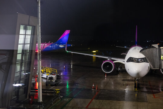 Bari, Italy, november 28, 2025. wizz air airplane boarding at night on a wet tarmac via a jet bridge in a moody airport setting, showcasing air travel and logistics after a rain shower