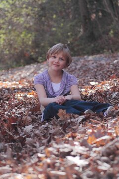 Smiling teenage girl wearing jeans sitting in a park amongst autumn leaves, USA