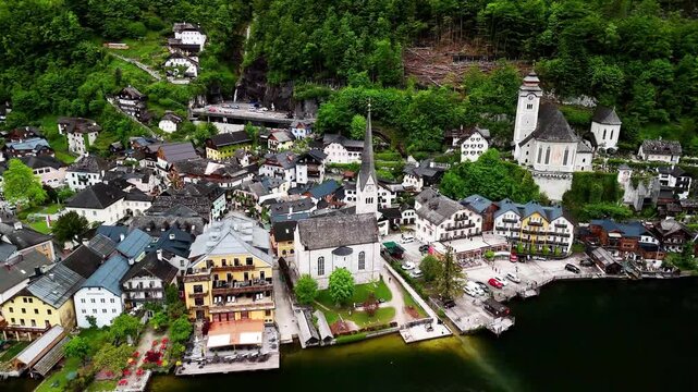 4K drone orbit of an alpine lakeside village on Lake Hallstatt, Austria. Church spires, colorful houses and waterfront revealed in a smooth circular flight over roofs, quay and forested slopes.