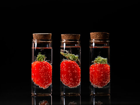 Close-up of tomatoes in three glass jars filled with liquid in front of a black background