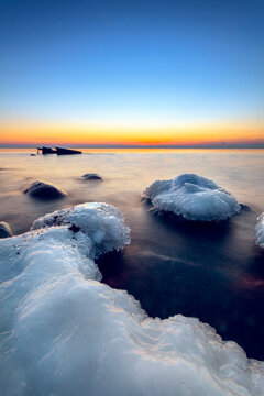 Distant shipwreck and Ice covered rocks on a winter beach at sunset, Lithuania