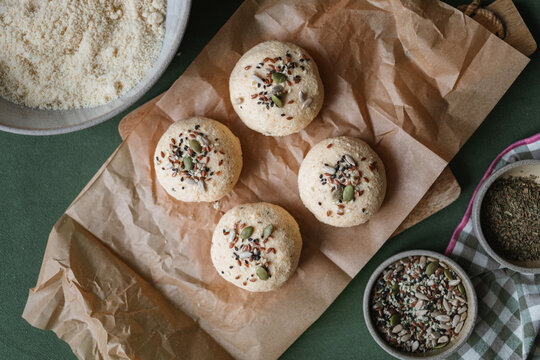 Overhead view of Low carb keto buns made with ricotta, almond and coconut flour and eggs topped with assorted seeds on a table with ingredients