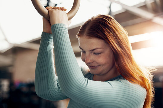 Smiling young woman with long red hair, holding a ring while working out in a gym.