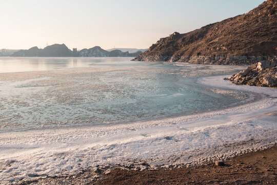 The freezing Kapchagai reservoir with hummocks of ice and mountains at sunset.