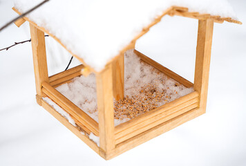 Wooden bird feeder filled with grain for birds in a winter garden. Cozy seasonal outdoor atmosphere. Selective focus.
