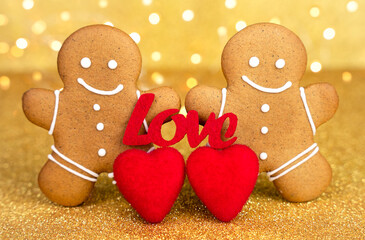 Cute gingerbread couple with red heart and word love on golden sparkling background. Romantic Valentine concept, sweet festive decoration. Close-up.