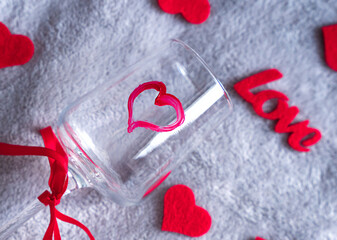 Wine glass decorated with a painted red heart surrounded by soft felt hearts and a love sign on a cozy gray background. Romantic Valentine's Day atmosphere. Selective focus.