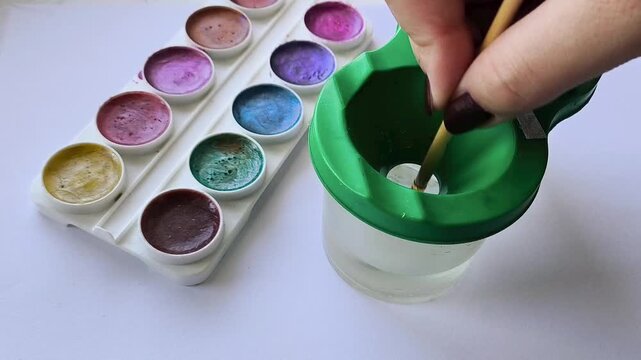 A woman's hand washes, dips the brush in spill proof watercolor. Drawing with an watercolour. Development, hobbies. Creative activities
