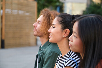 Obraz premium Three young students are sitting together and looking in the same direction, enjoying their free time in the city