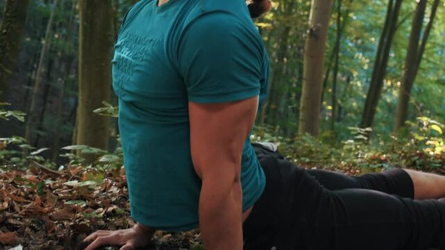 Bearded man practicing standing backbend yoga pose in sunny autumn forest. Young male stretching barefoot on fallen leaves at sunrise. Mindfulness and wellness in nature.