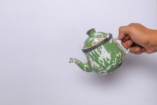 Close-up of Hand pouring classic Indonesian enamel teapot isolated on white background. Traditional teko blirik with vintage design for serving hot drinks. Cultural kitchenware concept