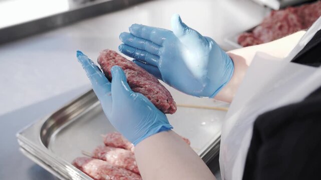 Professional chef in blue gloves preparing traditional raw meat kebab on skewer.
