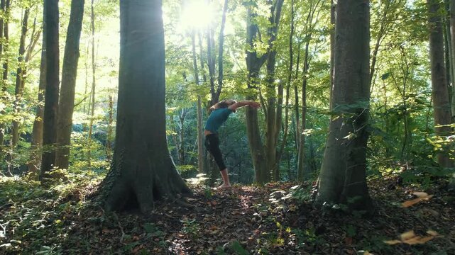 Man practicing yoga sun salutation and warrior pose in a sunny forest. Healthy lifestyle, mindfulness, and zen meditation in nature.