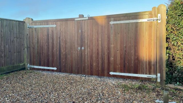 Panning shot of large wooden driveway gates and fence on a gravel driveway in morning sunlight